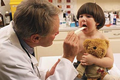 Doctor using tongue depressor on little boy with a bear in his arms