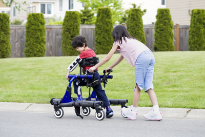 Girl pushing along her younger brother, who is a walking apparatus